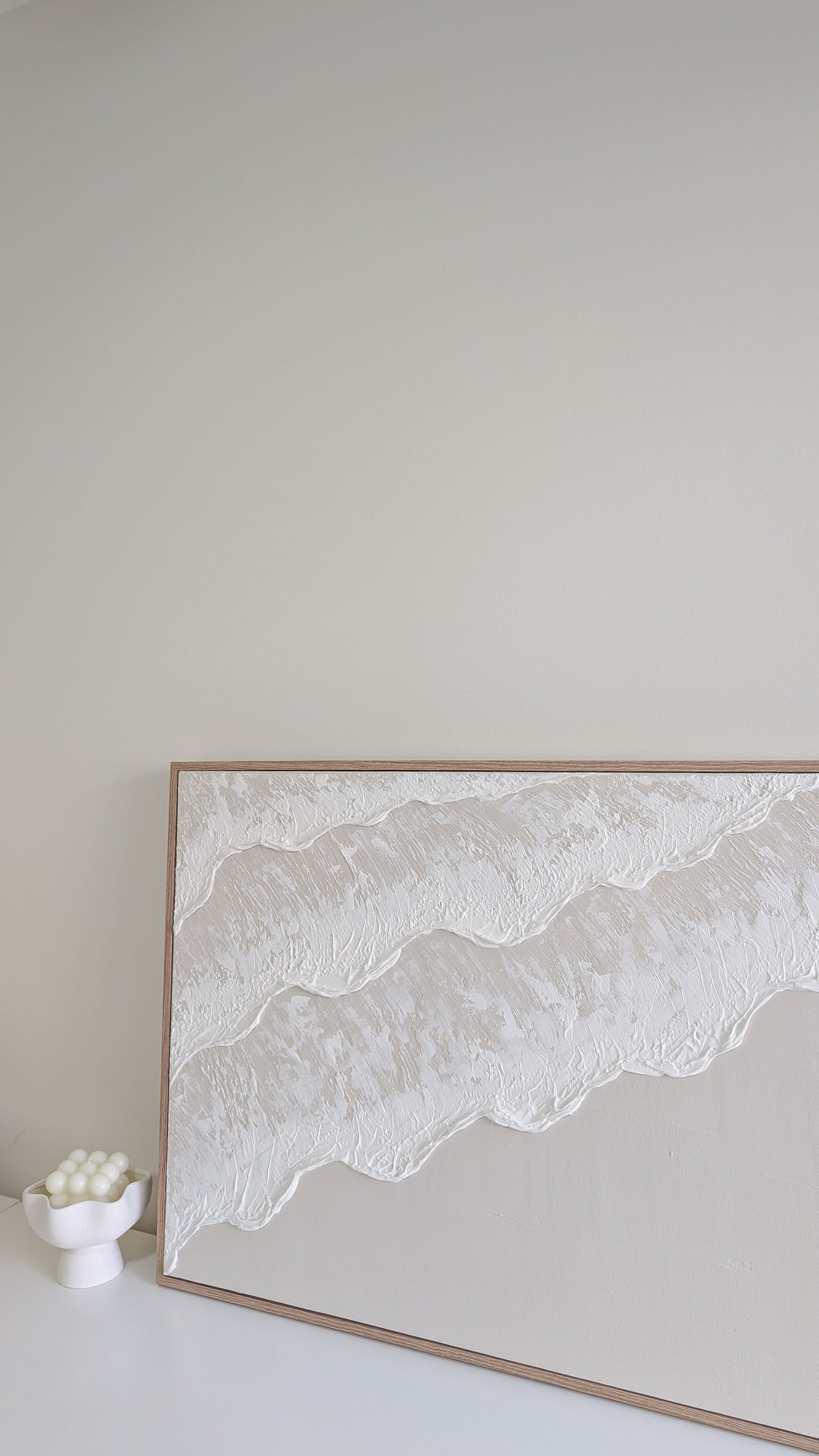 Framed artwork of wavy lines on a plain wall with a small white bowl below.