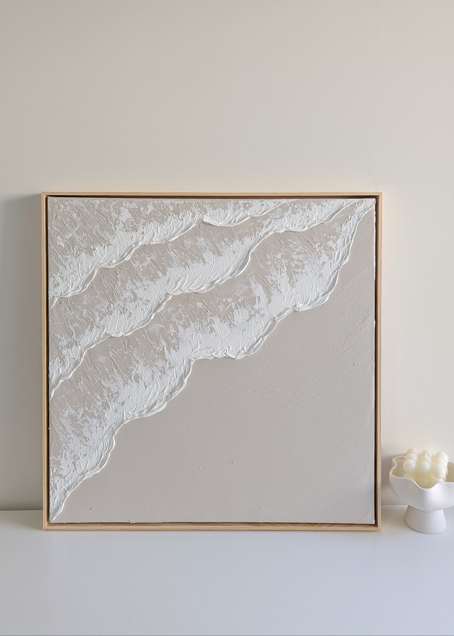 Framed neutral colour ocean wave artwork on a plain wall