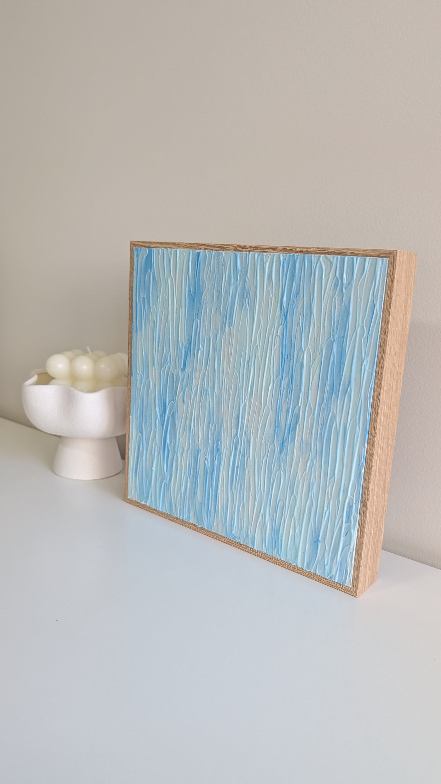 Abstract art piece with blue and white patterns in a wooden frame on a light surface.