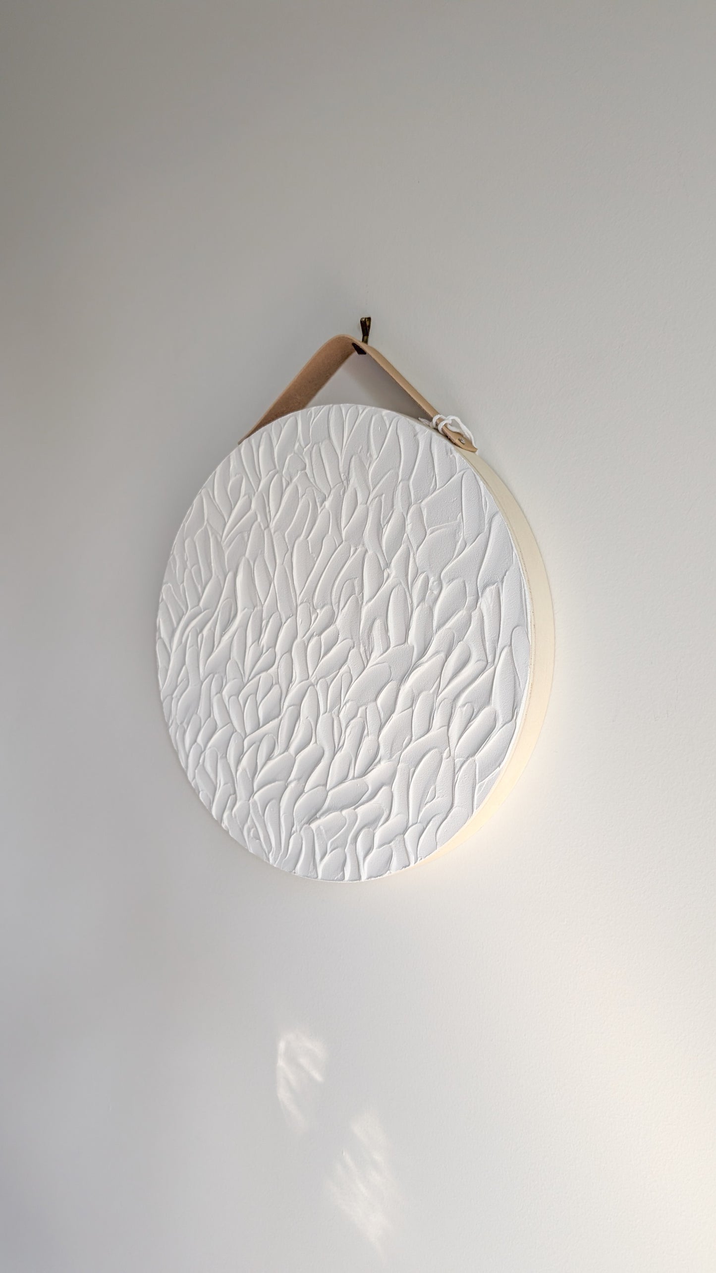 pure white textured art leaf stroke design on a round wood panel hanging on a light grey wall background