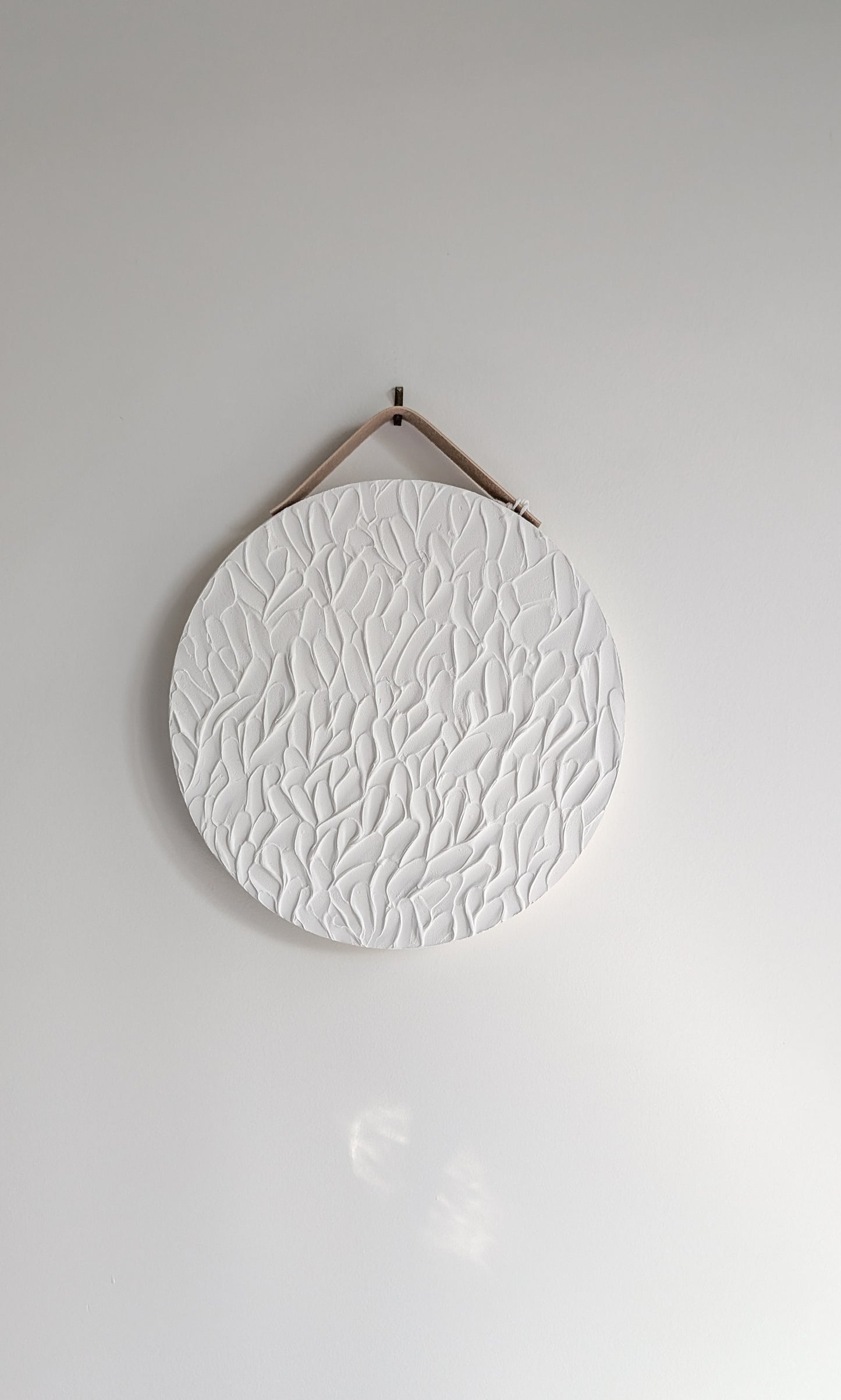 Minimalist round white textured art piece with organic leaf-inspired patterns, hanging on a neutral wall with soft natural light – handmade artwork by Christen Rose.