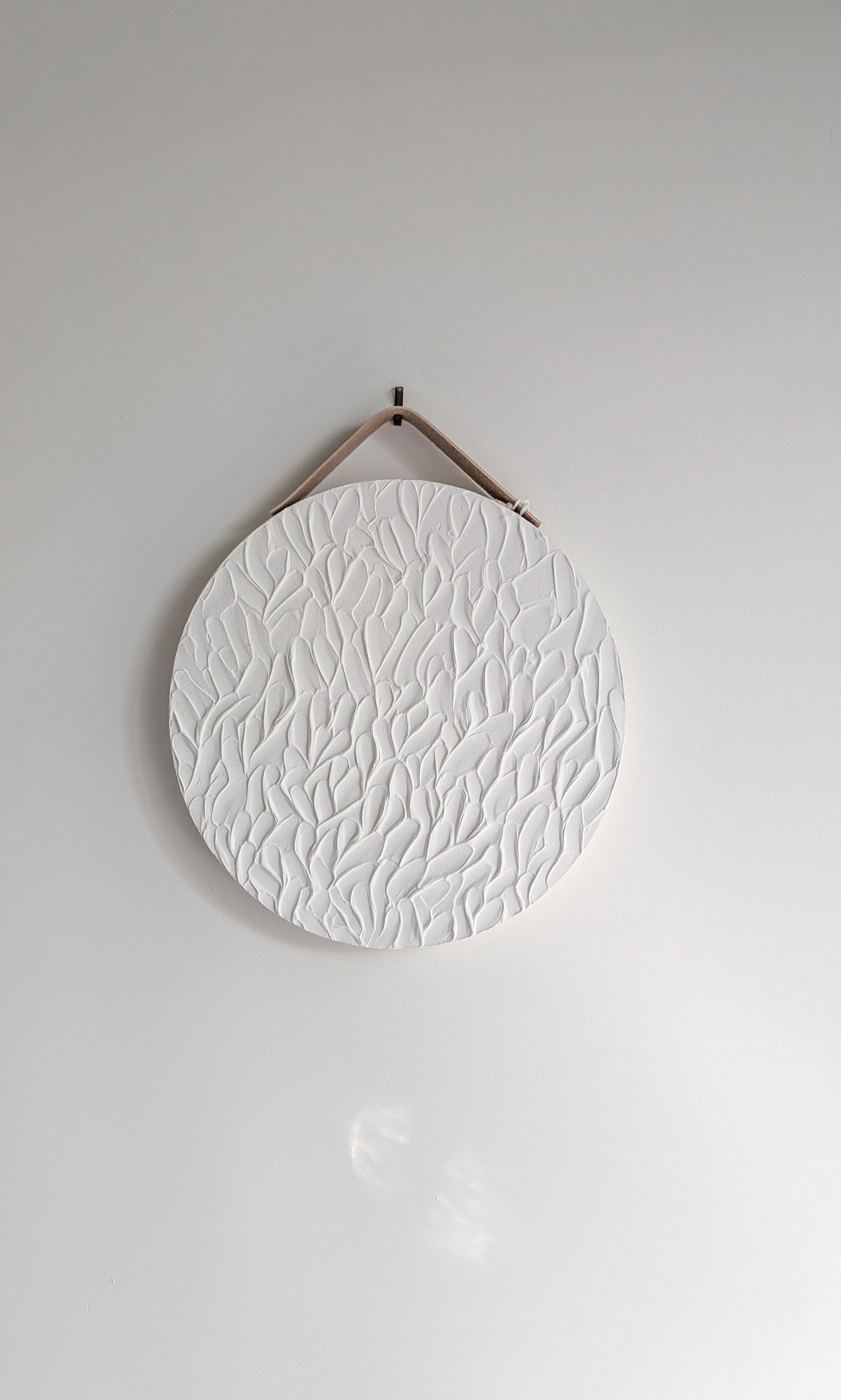 Minimalist round white textured art piece with organic leaf-inspired patterns, hanging on a neutral wall with soft natural light – handmade artwork by Christen Rose.