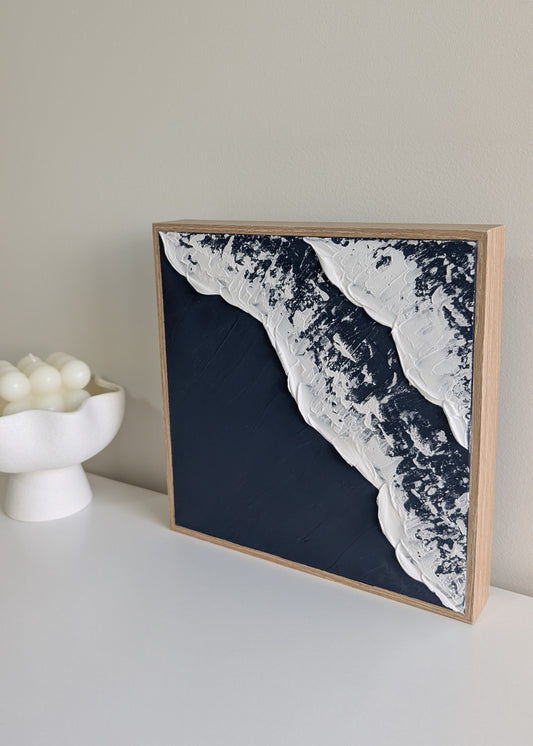 Framed artwork with a navy and white abstract ocean waves design on a light surface.