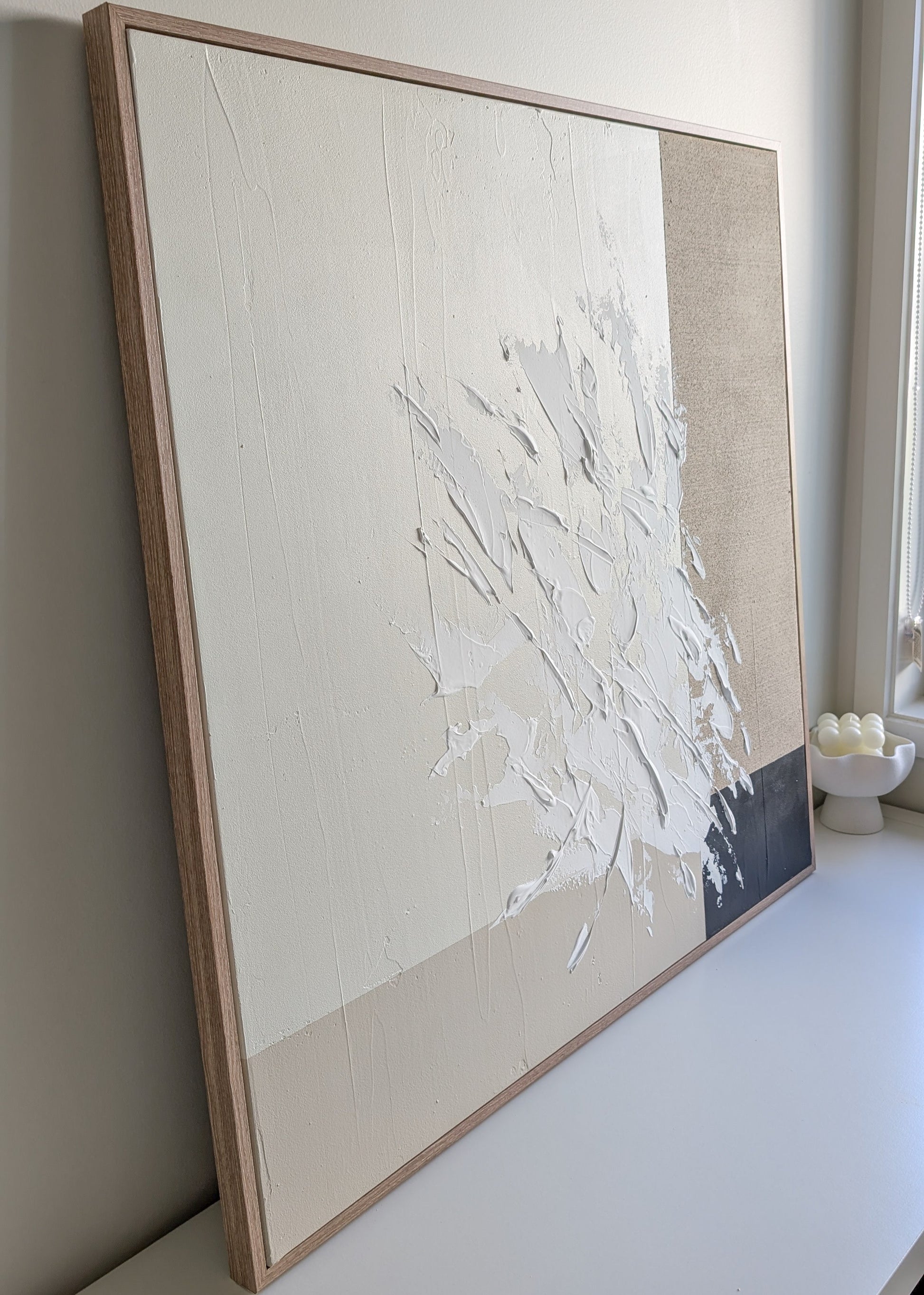Abstract art piece in a wooden frame on a white wall