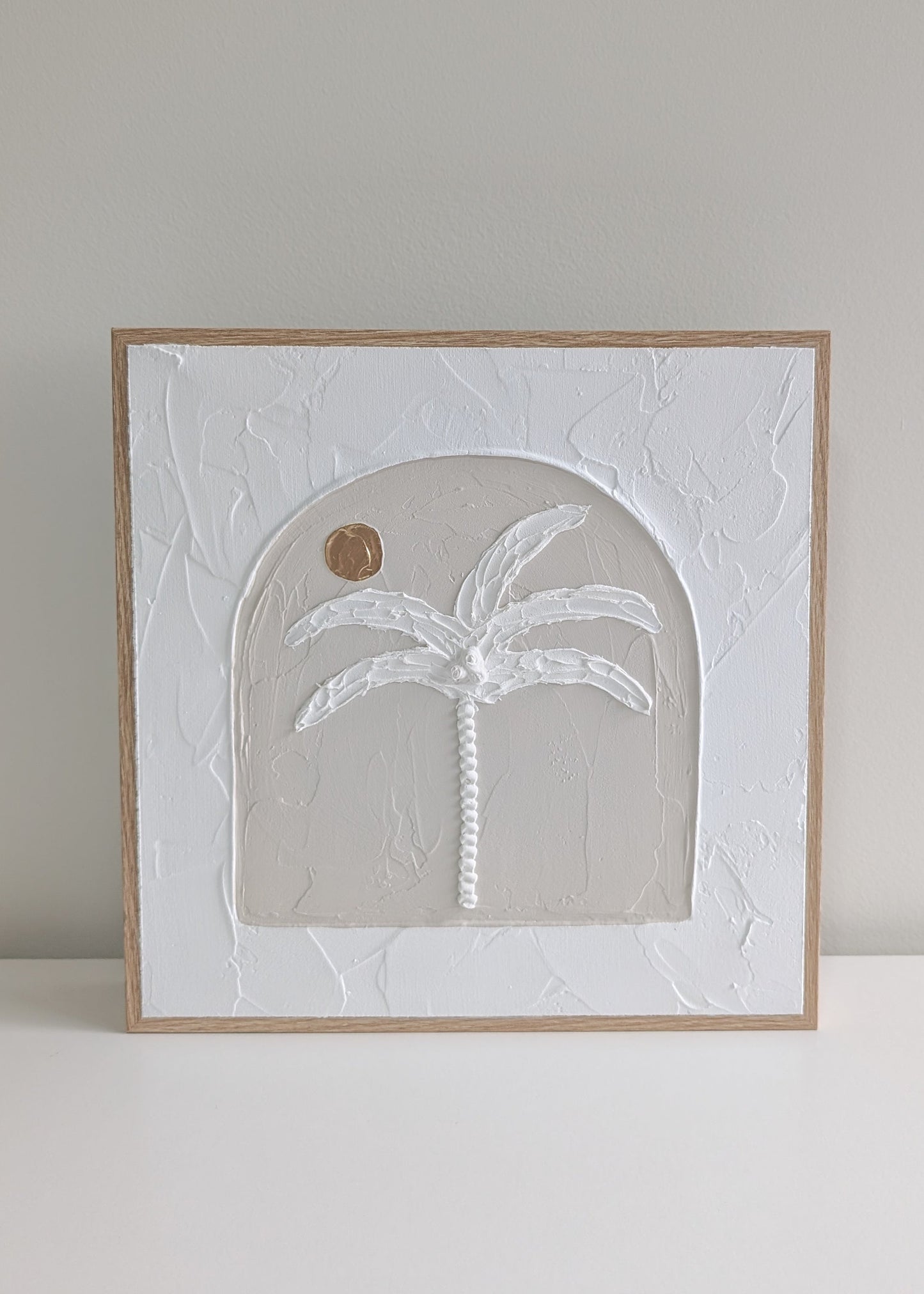 Handmade neutral palm tree textured wall art in arched design, framed in natural timber, angled view