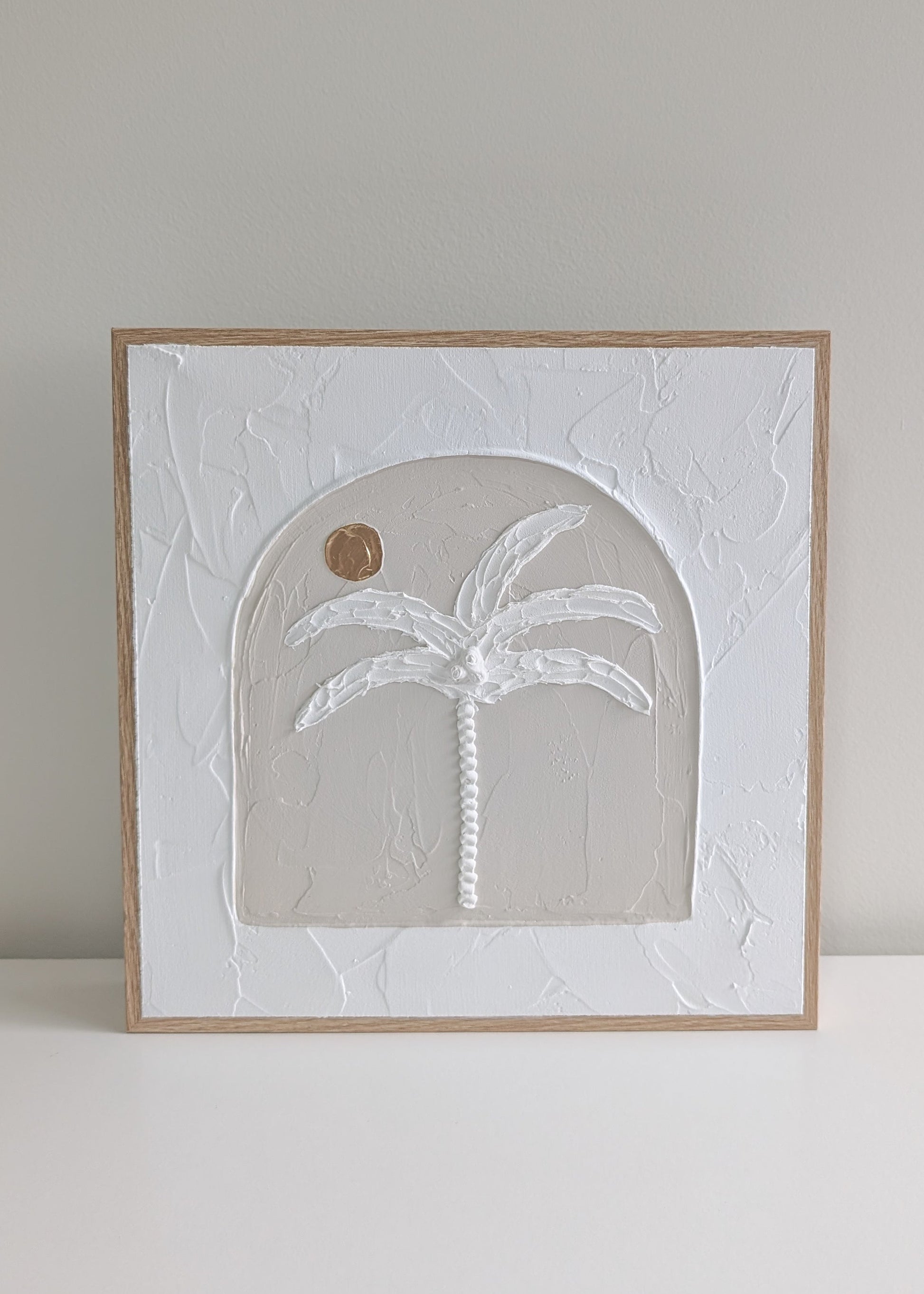 Handmade neutral palm tree textured wall art in arched design, framed in natural timber, angled view