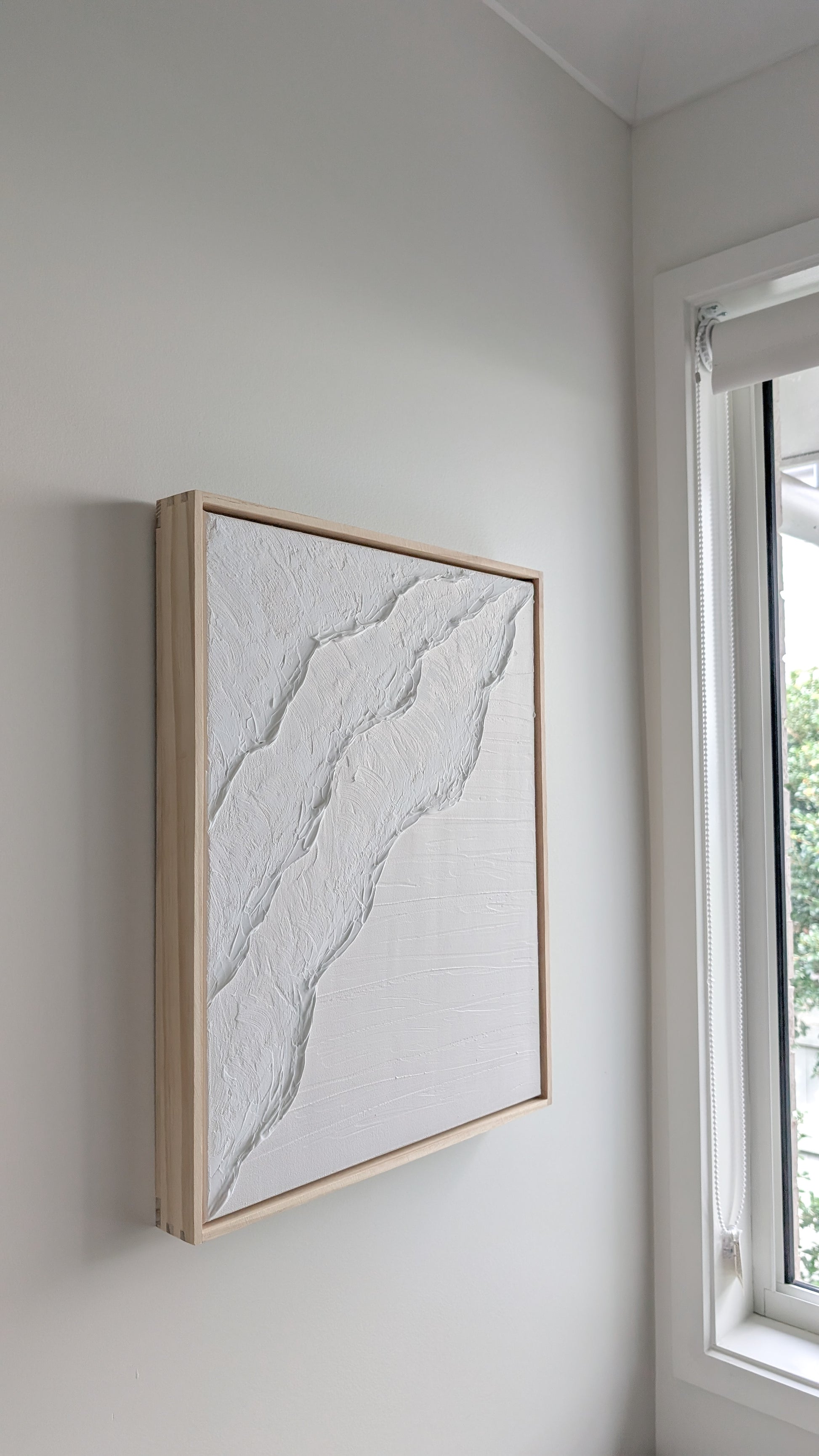 White textured coastal wall art with organic flowing design, framed in natural pinewood and displayed near a bright window – handmade by Christen Rose