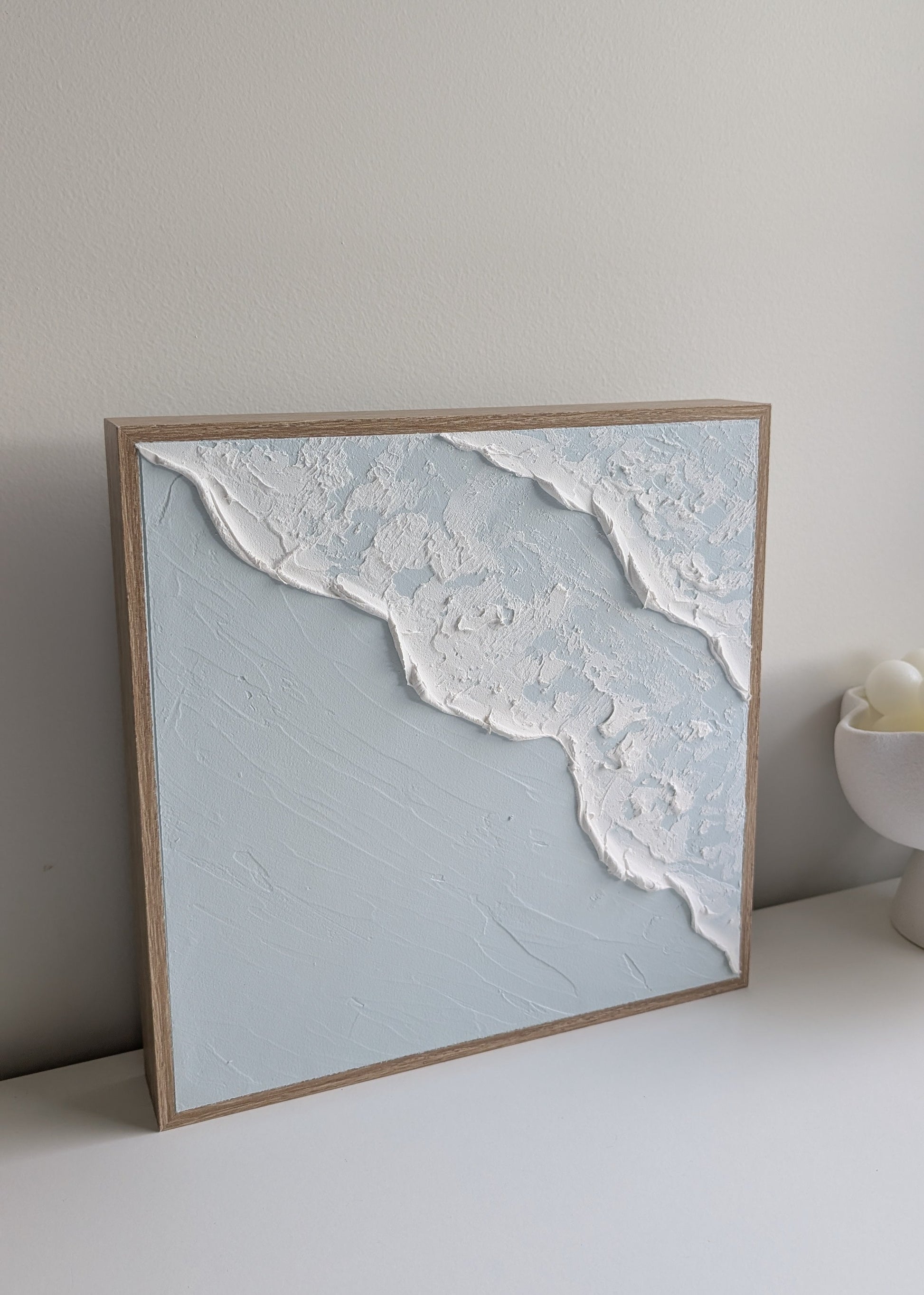 Handmade coastal wave textured wall art with natural timber frame, angled view against white wall