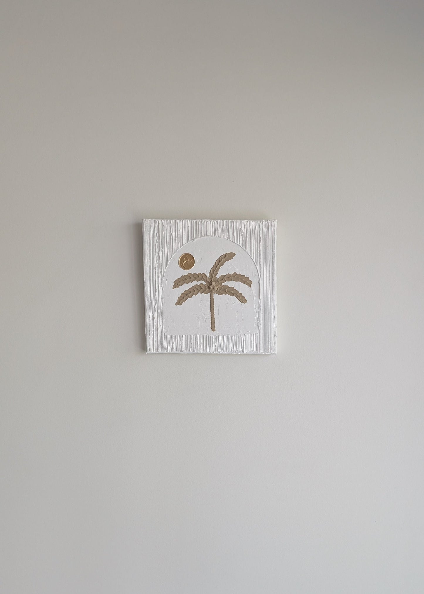 Small square wall art with a palm tree design on a plain wall