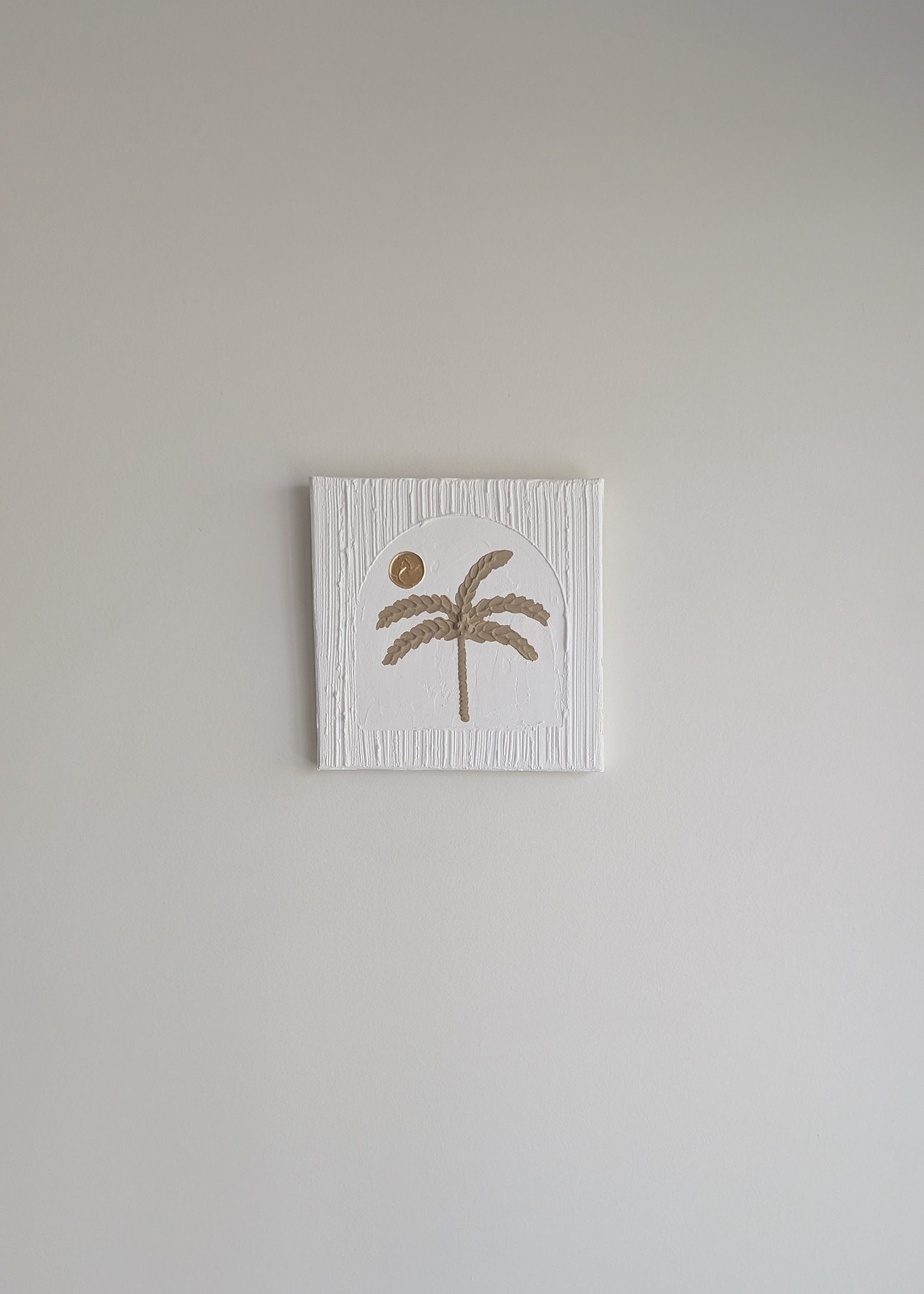 Small square wall art with a palm tree design on a plain wall