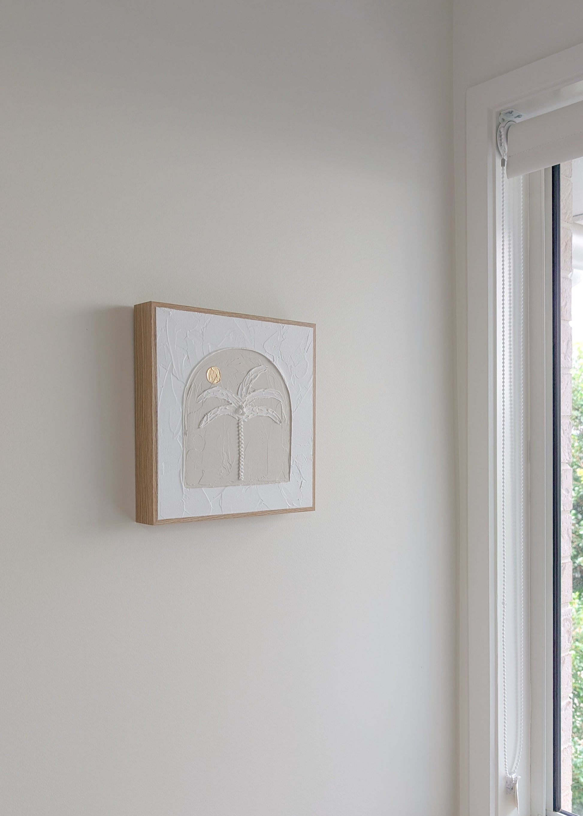 Palm tree textured coastal wall art hanging on white wall near window