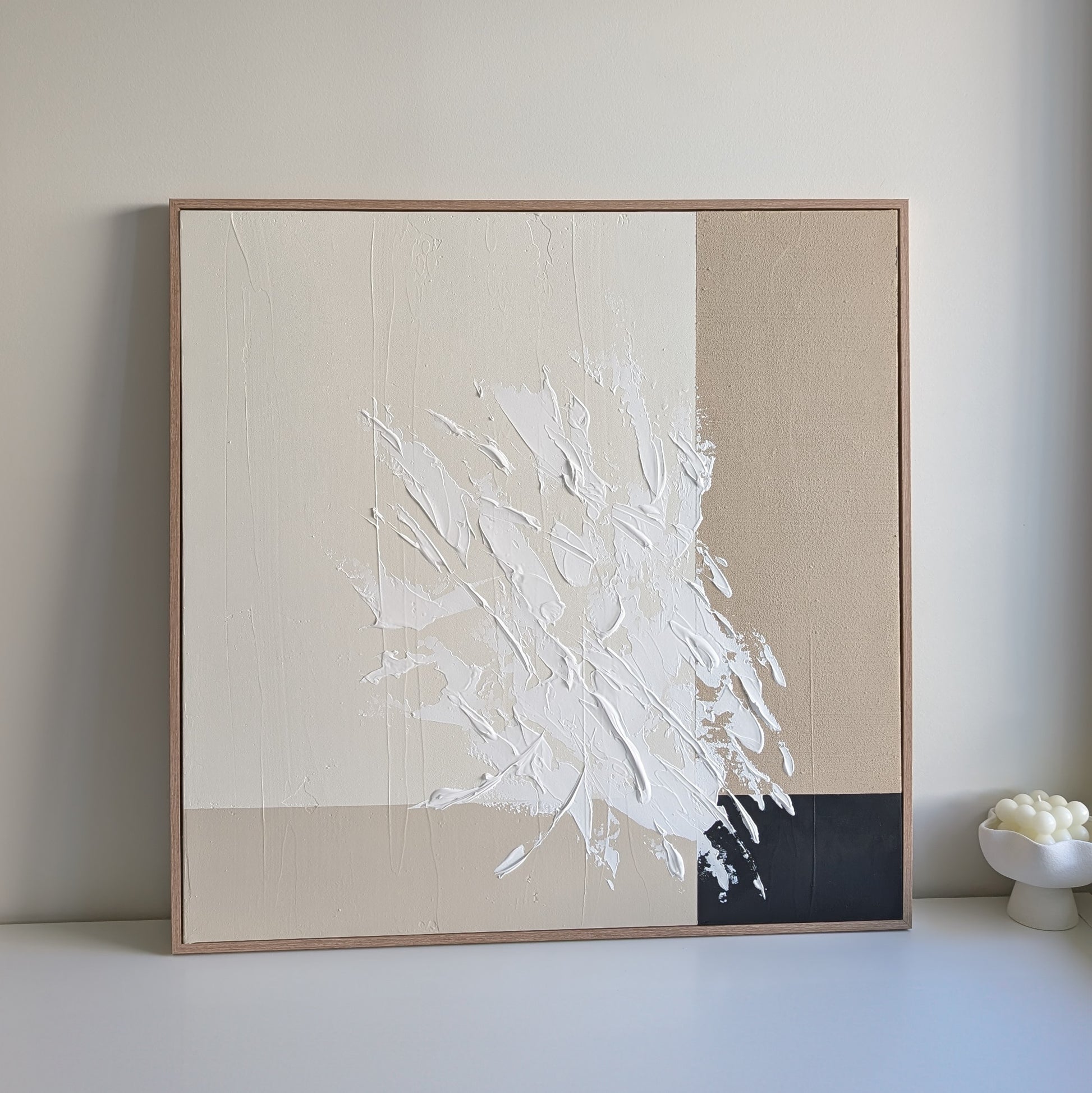 Abstract art piece with white brush strokes on a beige background, framed in a light wood color.
