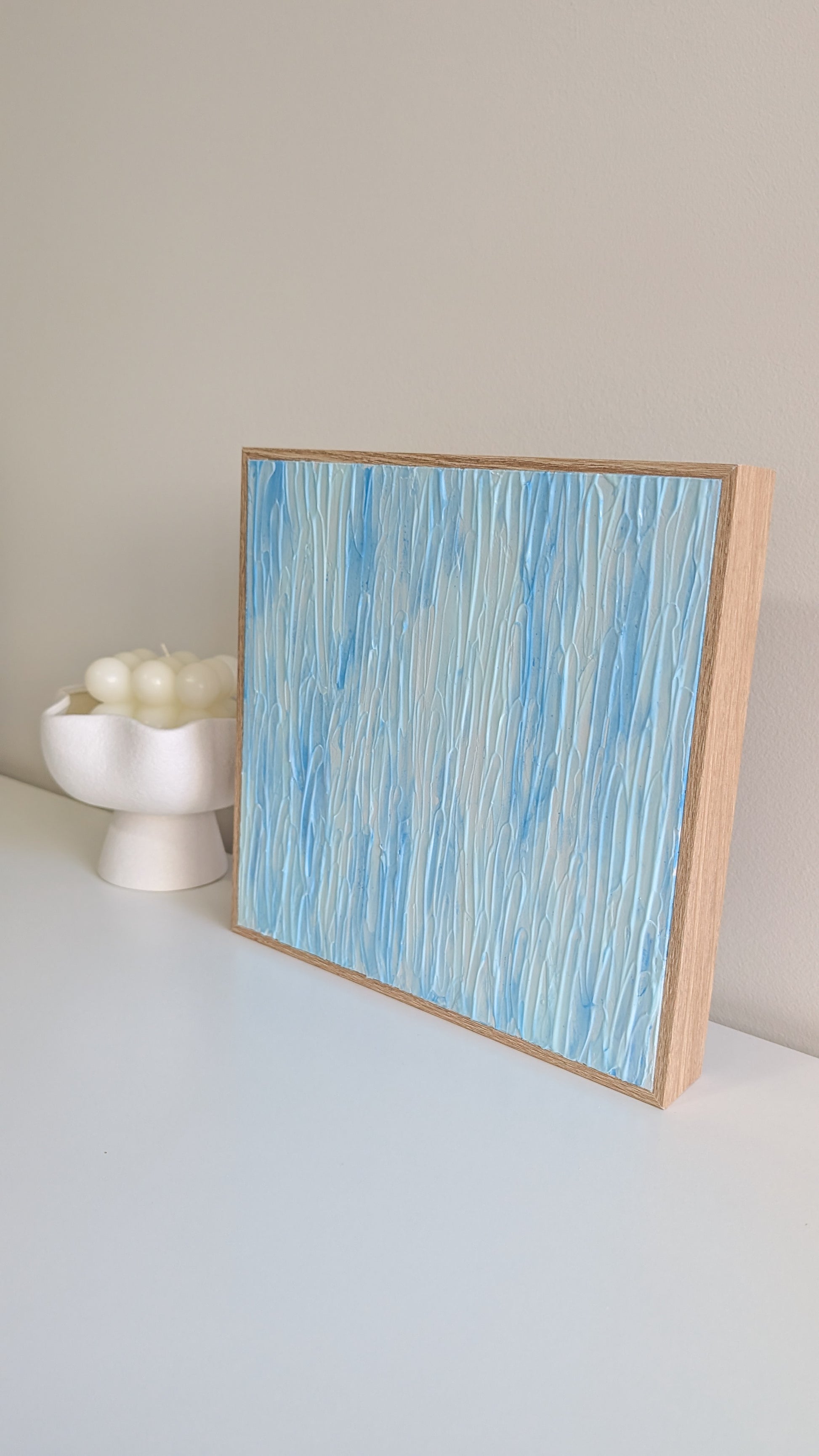 Abstract art piece with blue and white patterns in a wooden frame on a light surface.
