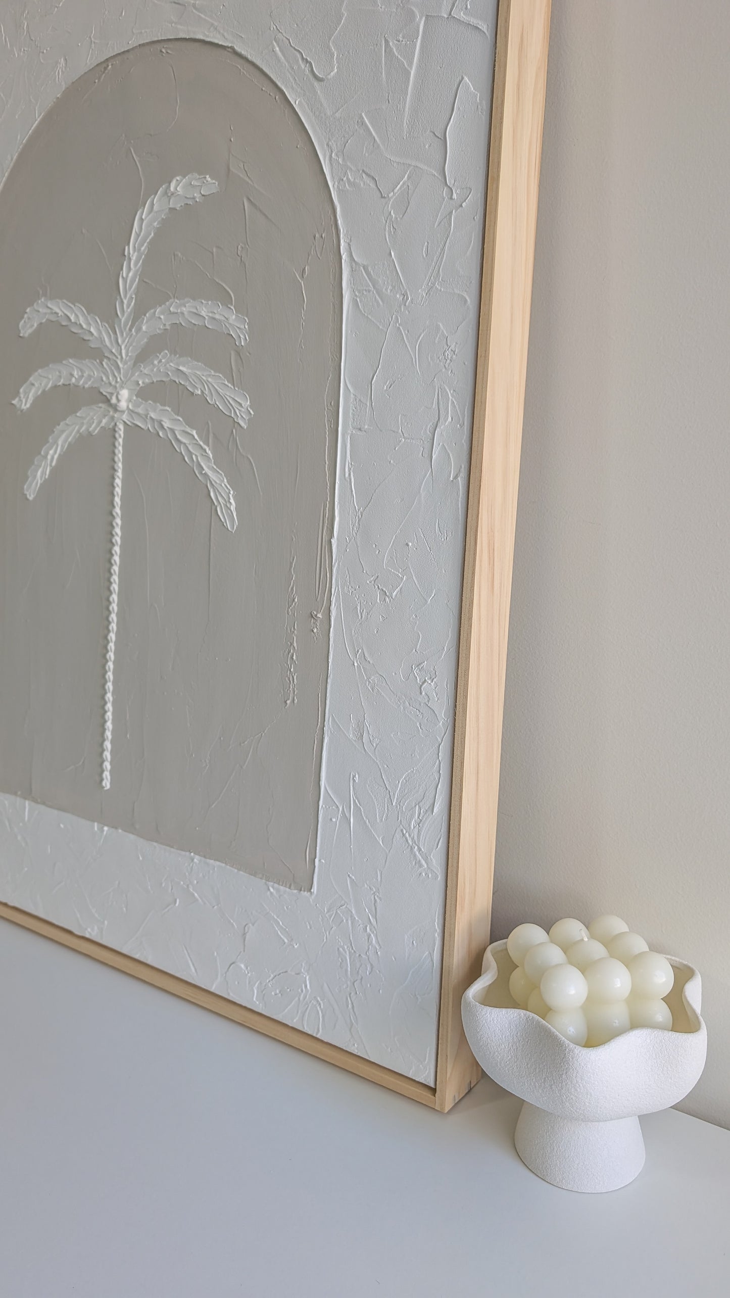 Close-up of handmade textured palm tree artwork showing raised plaster details and smooth arched background in soft coastal tones.