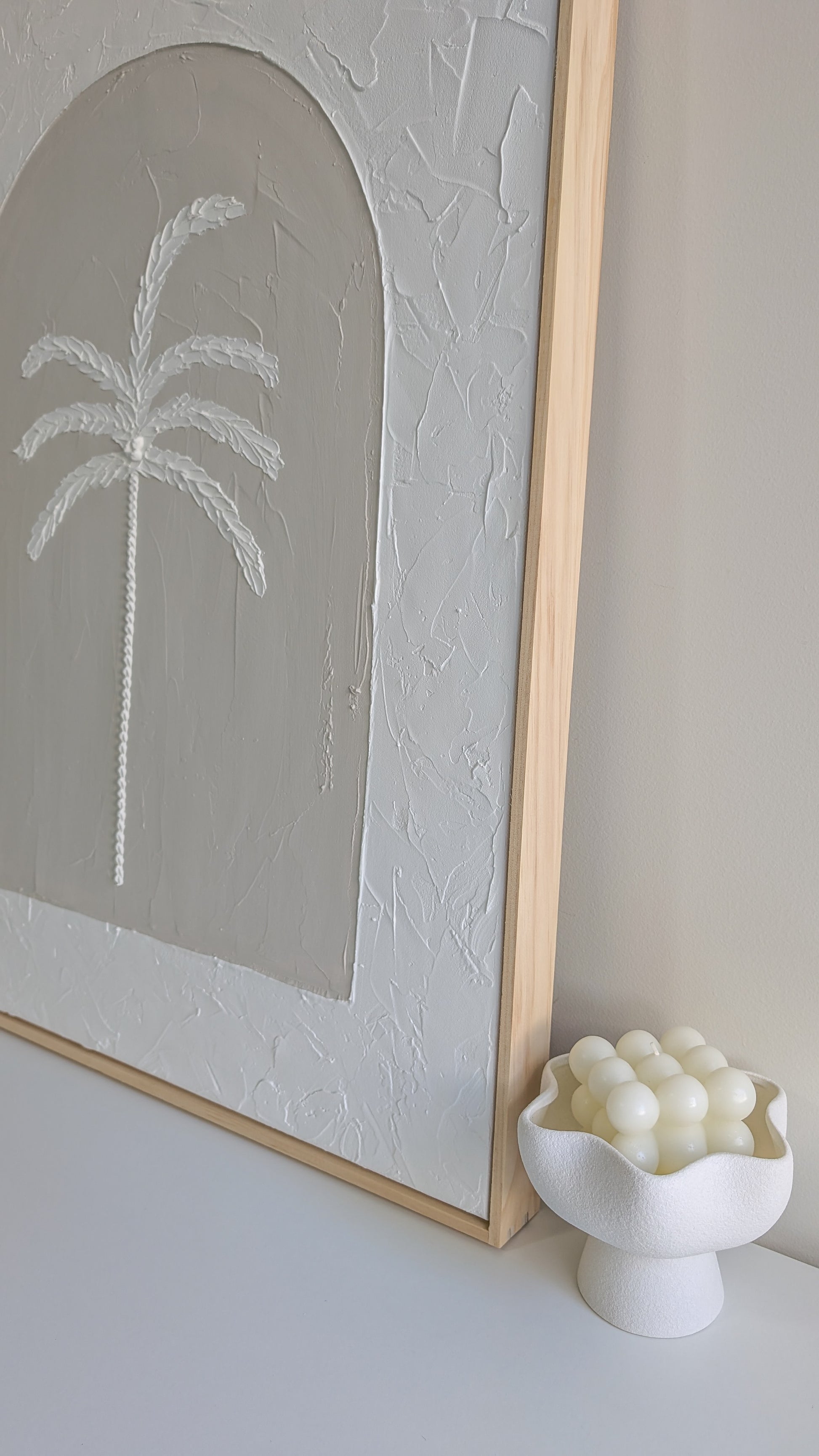 Close-up of handmade textured palm tree artwork showing raised plaster details and smooth arched background in soft coastal tones.