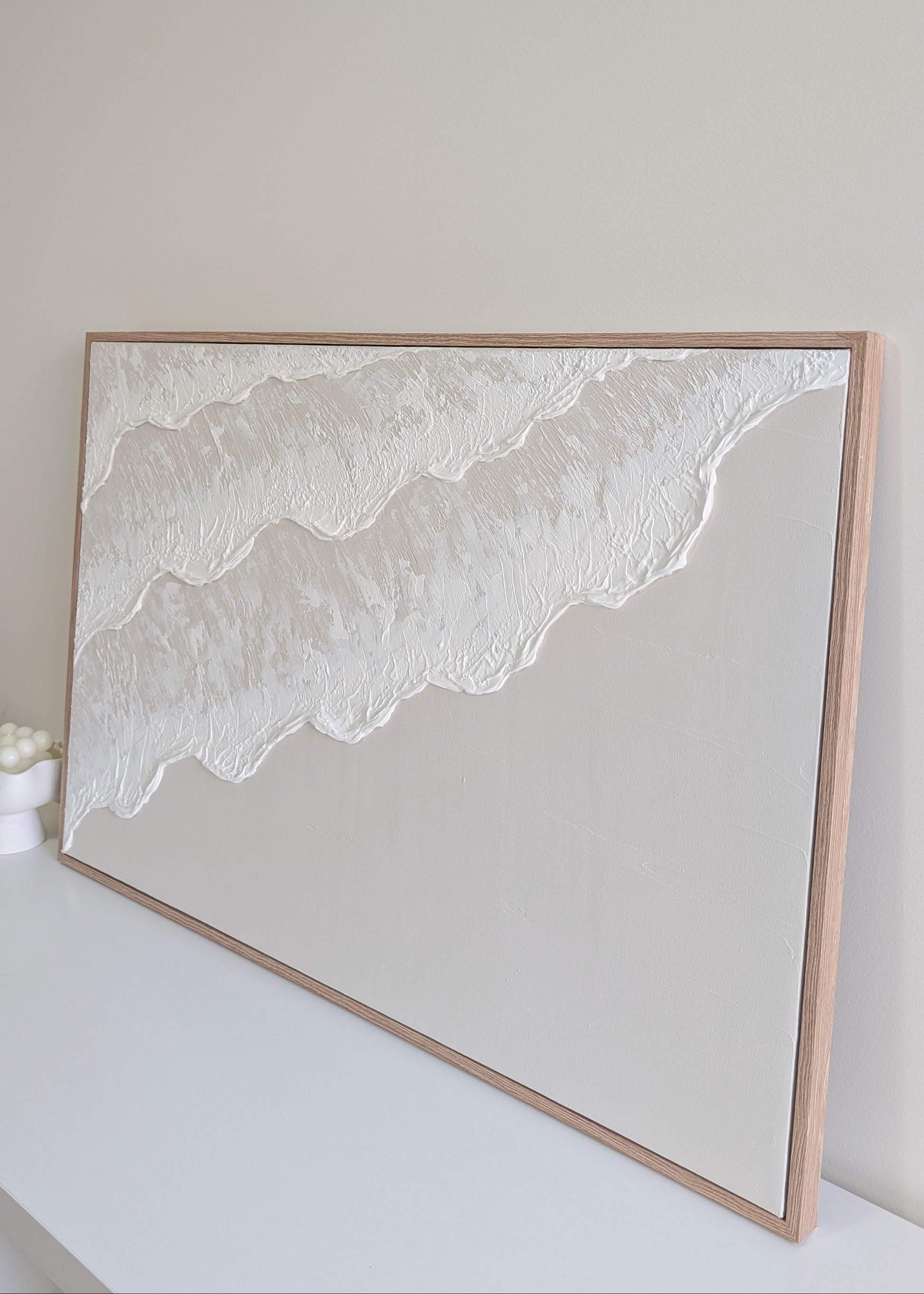 light beige ocean wave design artwork finished in a oak frame on a white wall