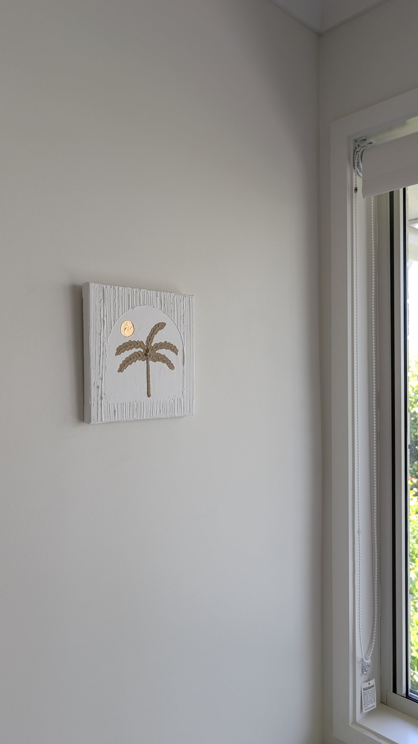 Palm tree painting on a wall next to a window with a view of greenery