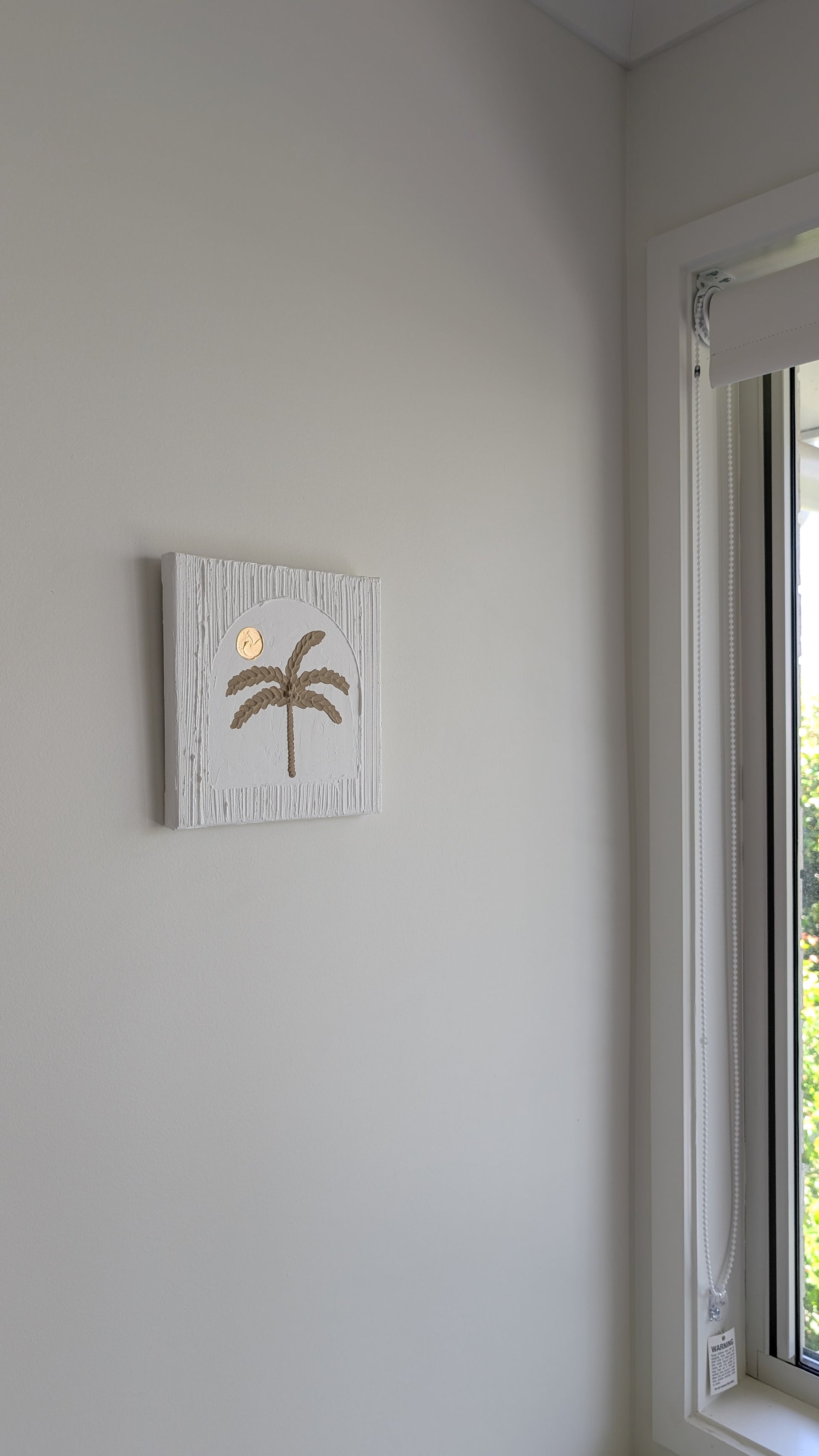 Palm tree painting on a wall next to a window with a view of greenery