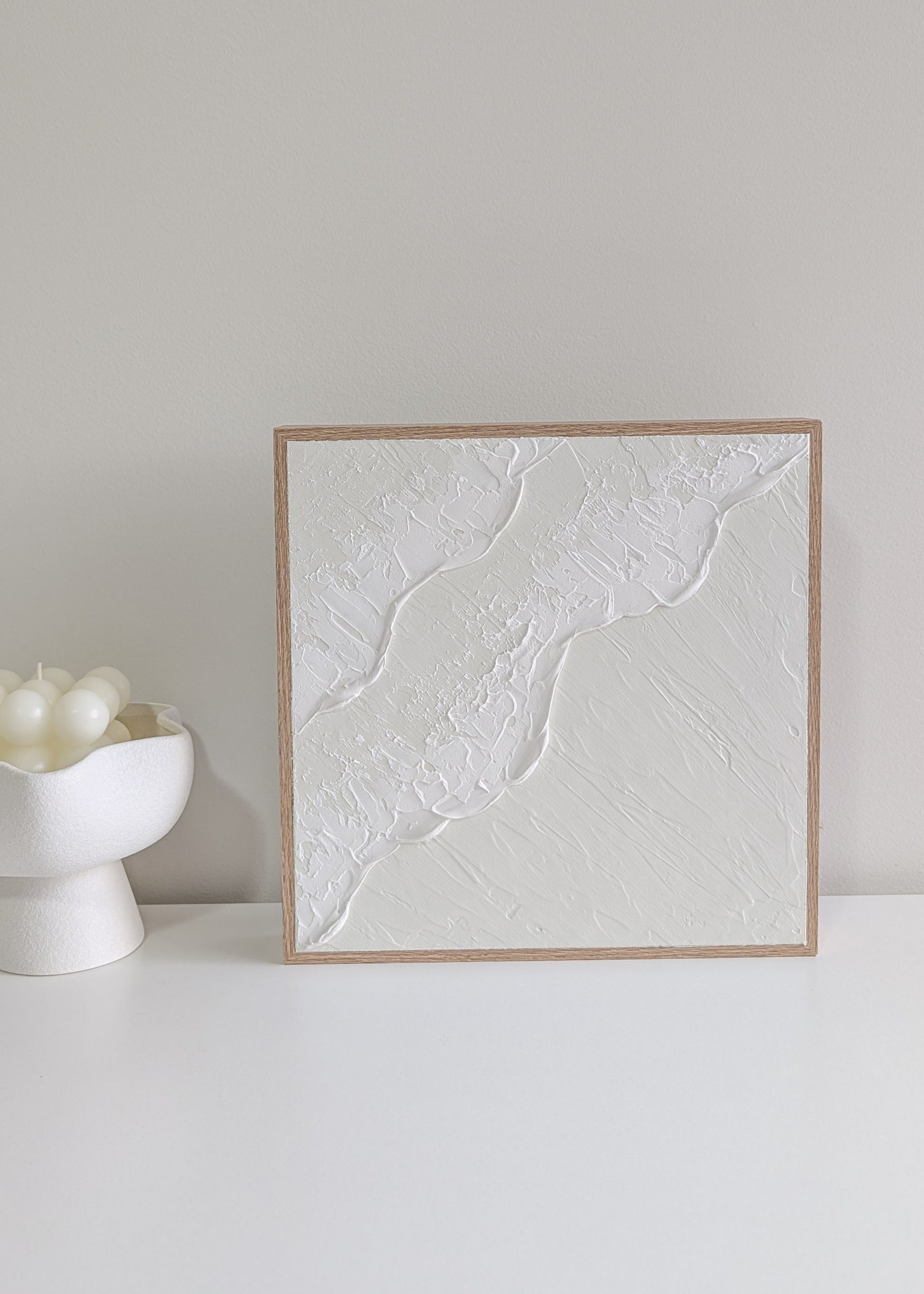 Framed textured artwork on a white surface with a neutral background