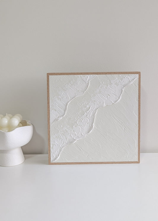 Framed textured artwork on a white surface with a neutral background