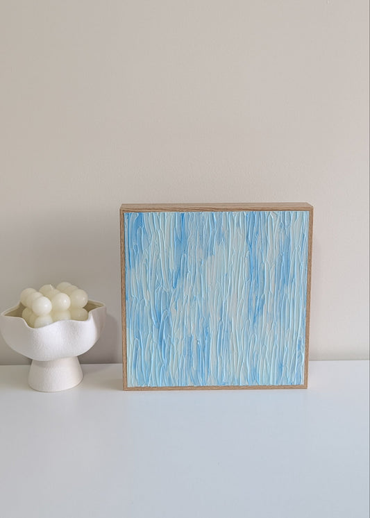 Framed abstract blue artwork on a white surface with a neutral background