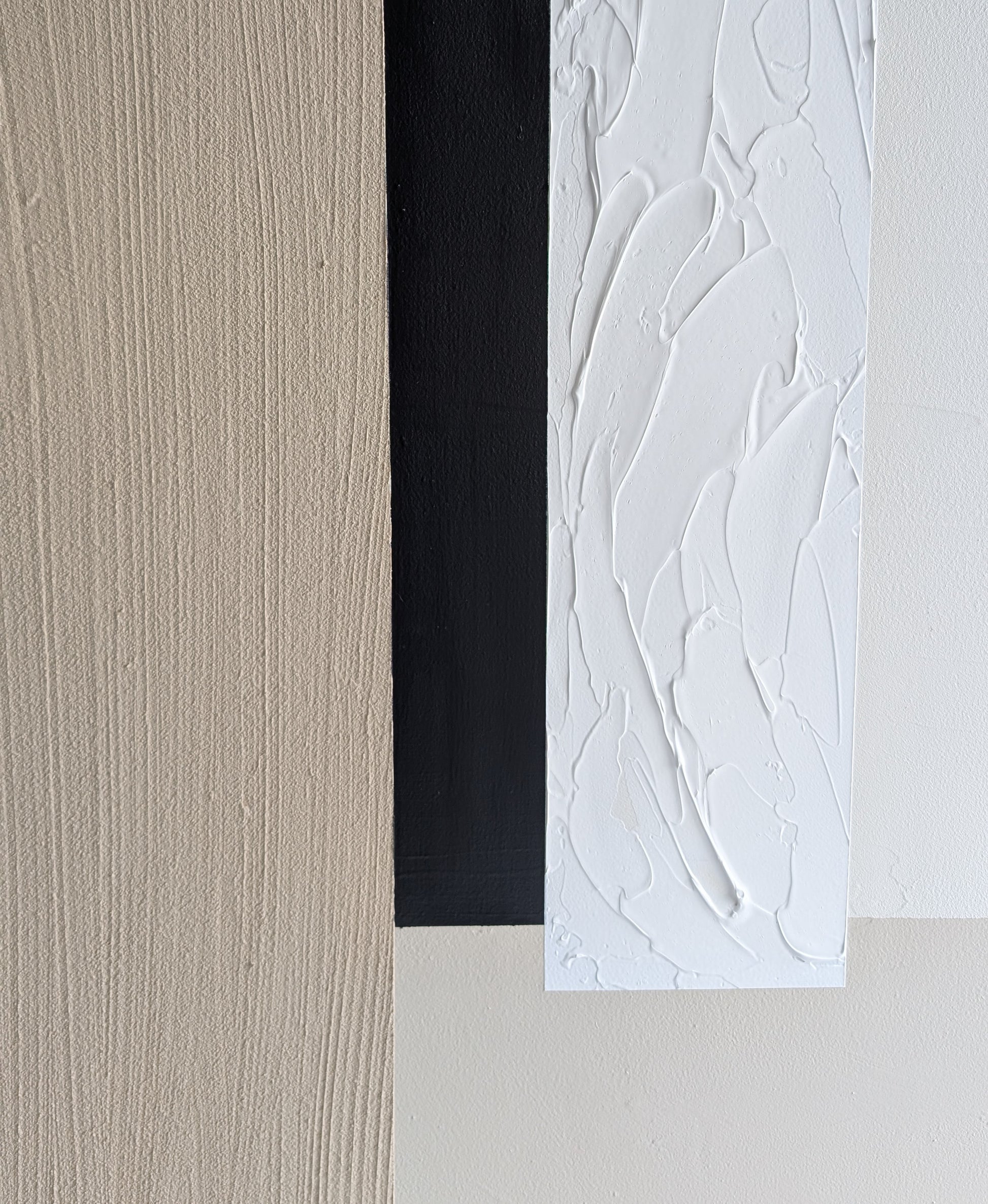 Close-up of textured wall art in beige, black, and white.