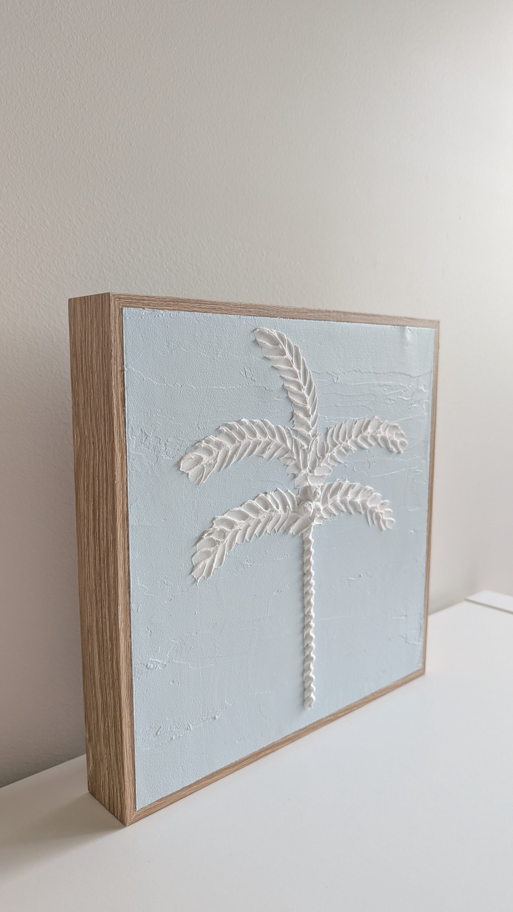 Side profile of blue palm tree textured artwork showing raised palm design and wood-look frame