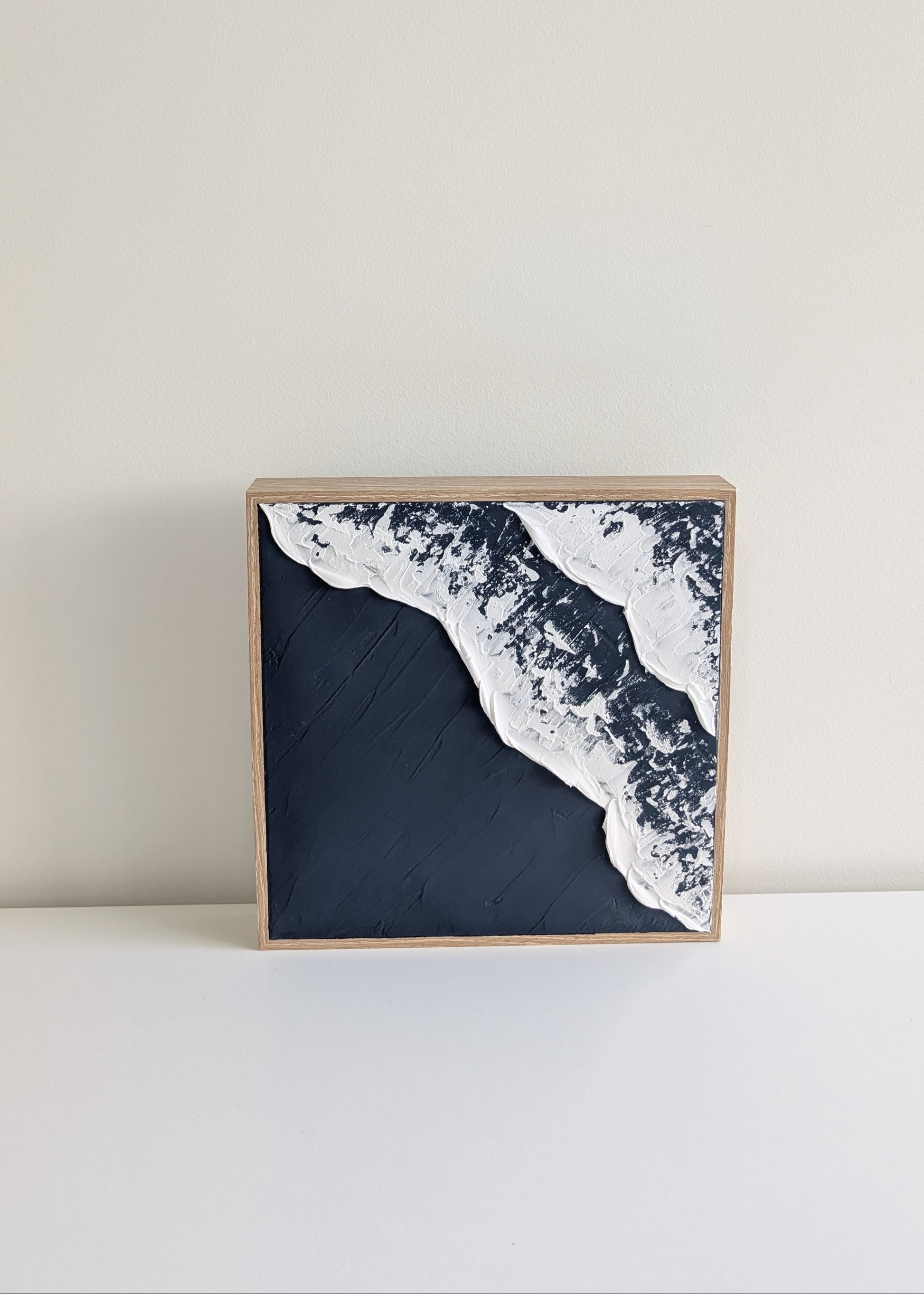 Square framed artwork of a wave on a plain background