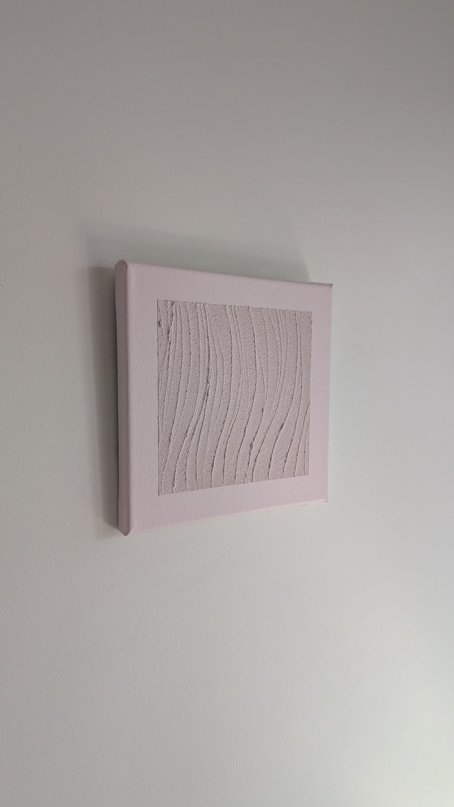 Textured wall art in a pink frame on a plain white wall