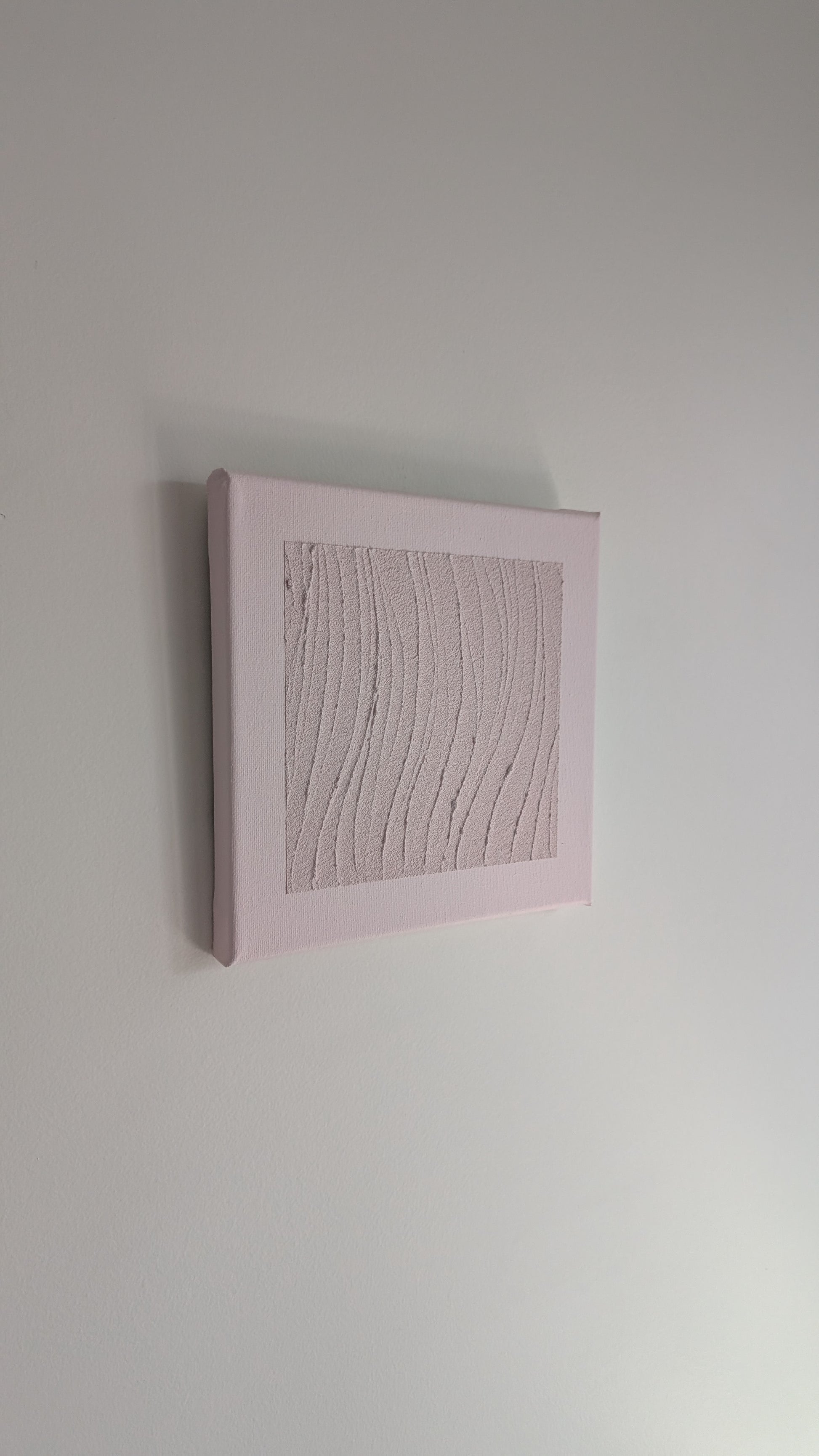 Textured wall art in a pink frame on a plain white wall