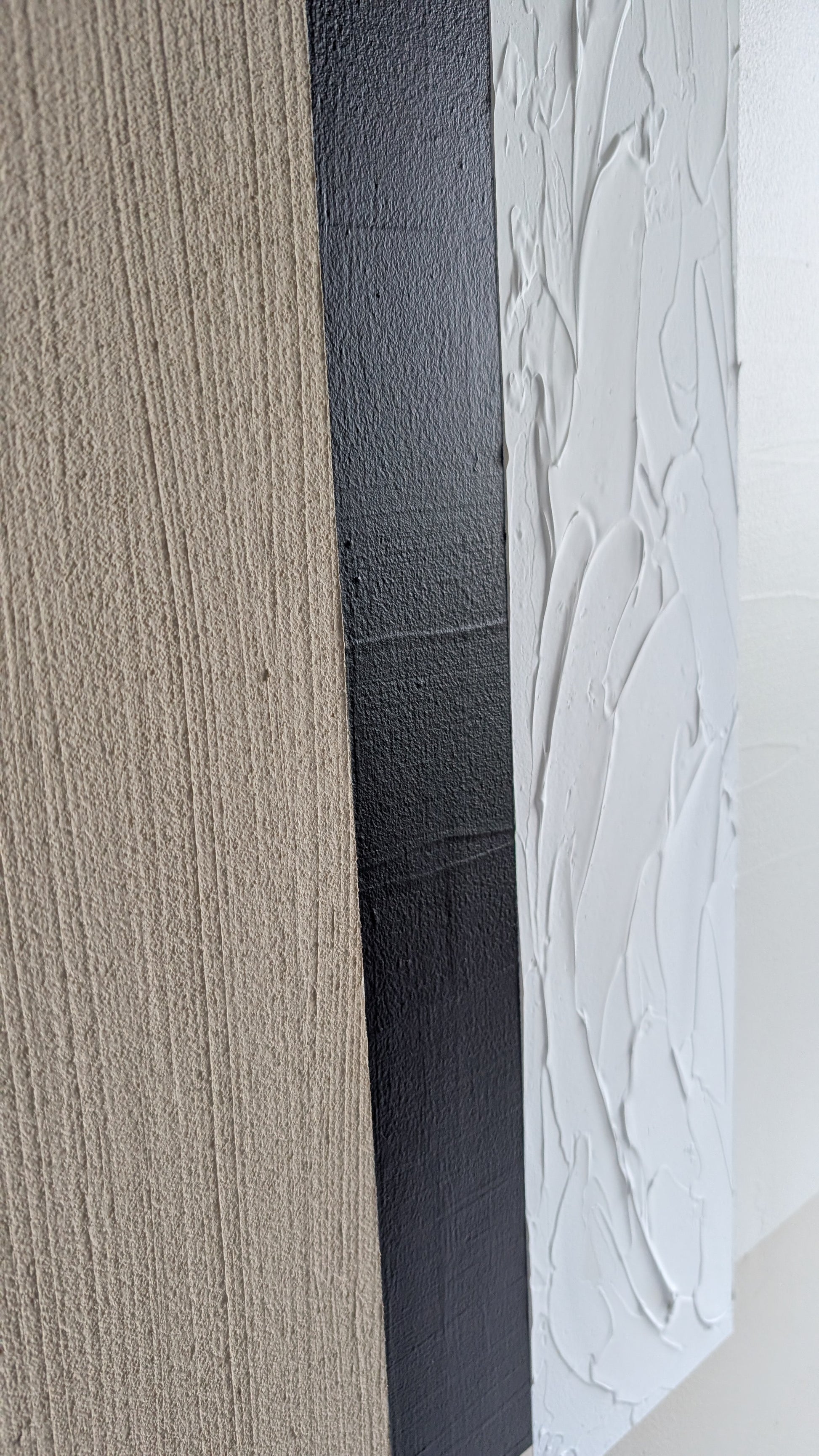 Close-up of textured wall art in beige, black, and white.