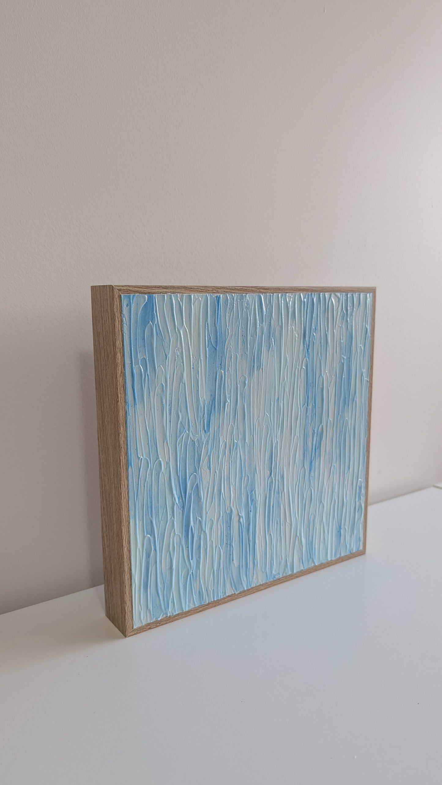 Abstract painting with blue and white patterns in a wooden frame on a light gray surface.