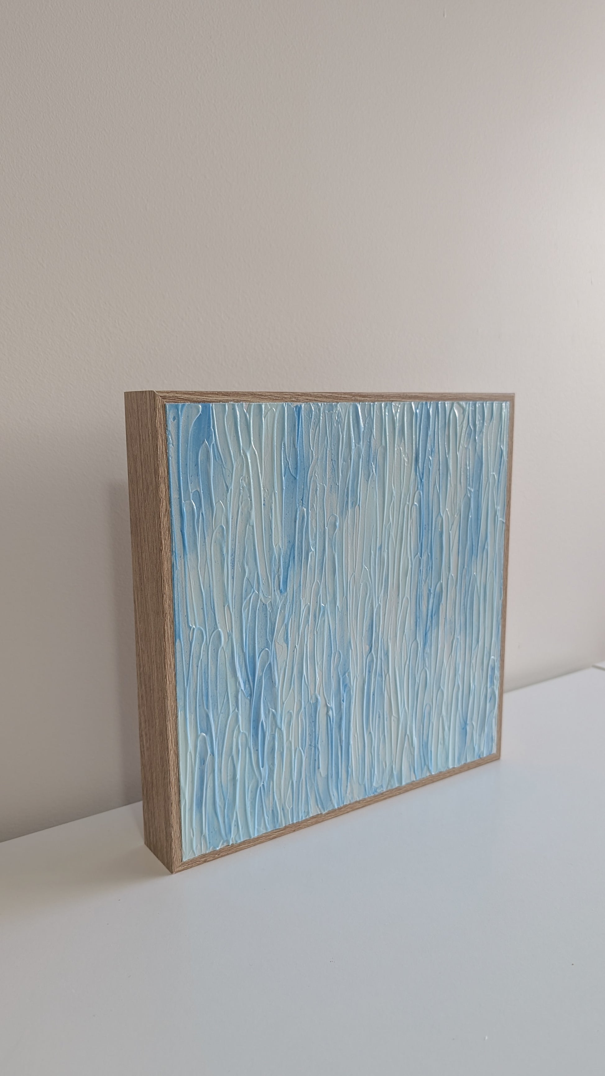 Abstract painting with blue and white patterns in a wooden frame on a light gray surface.