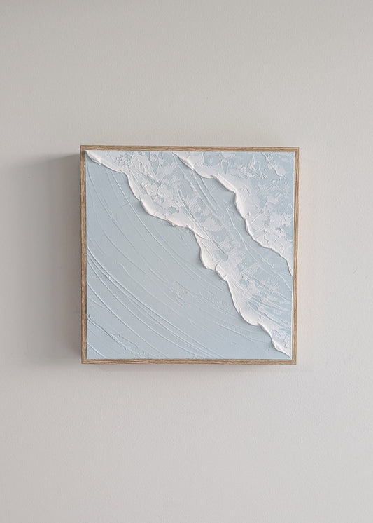 Framed artwork of a beach scene with waves on a light gray wall