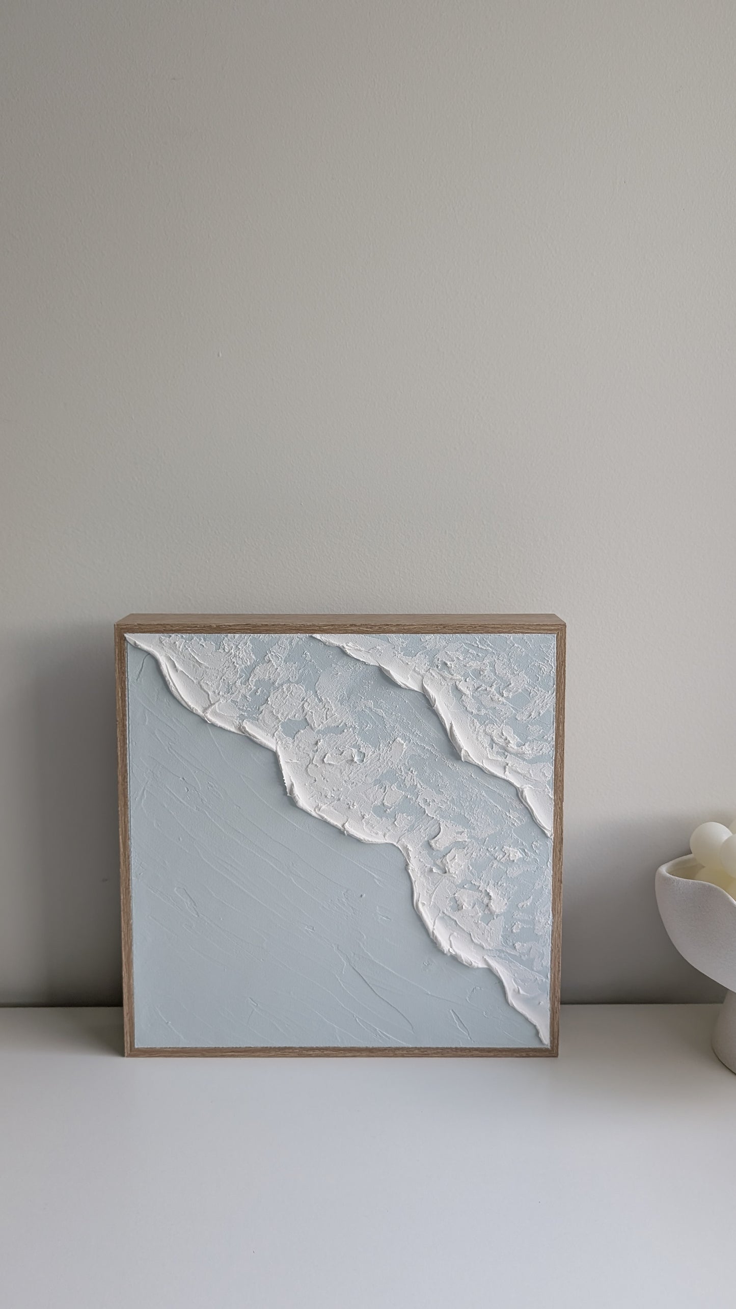 Ocean-inspired textured wall art featuring white wave detail on blue background, straight-on view